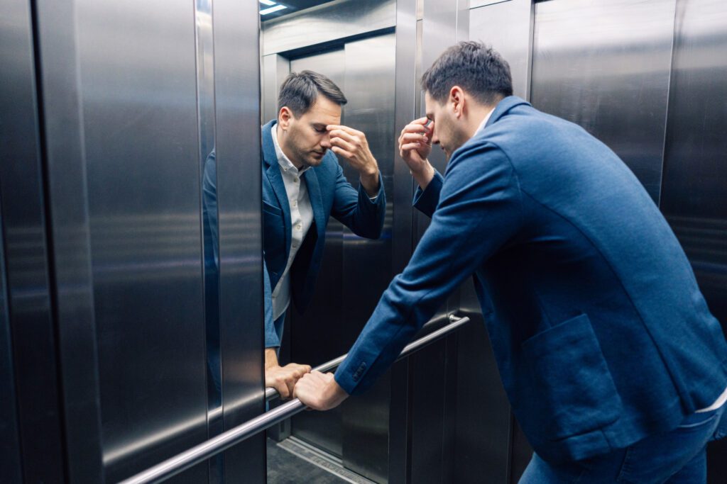 Man in elevator touching forehead, looking stressed.